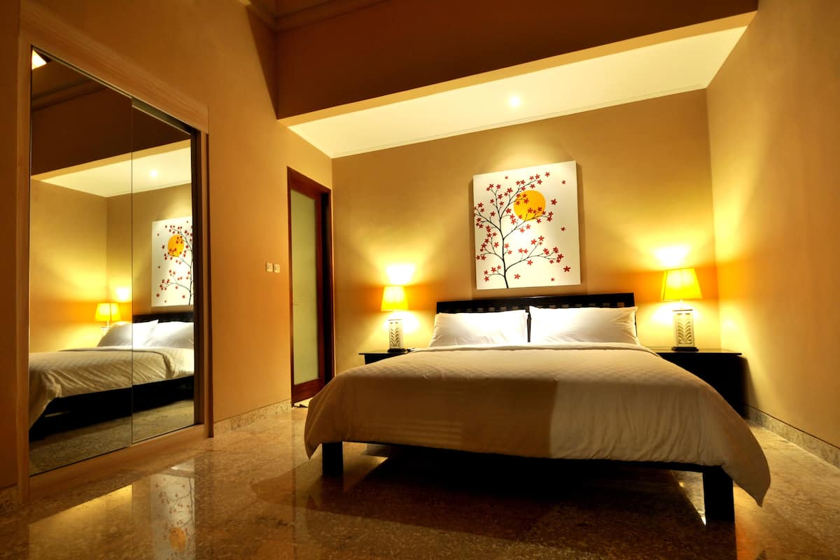 A hotel room with a large bed, two bedside tables with lamps, a mirror, and a wall-mounted artwork.