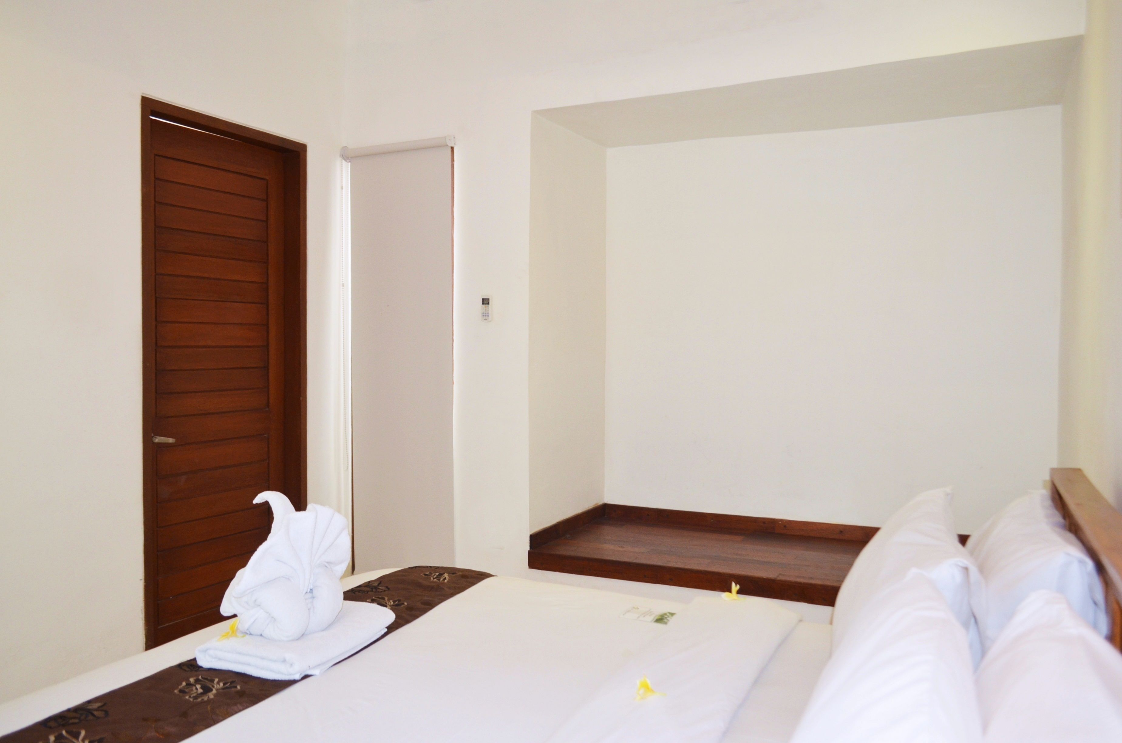 A hotel room with a wooden door, a bed with white linens, and a small wooden nightstand.
