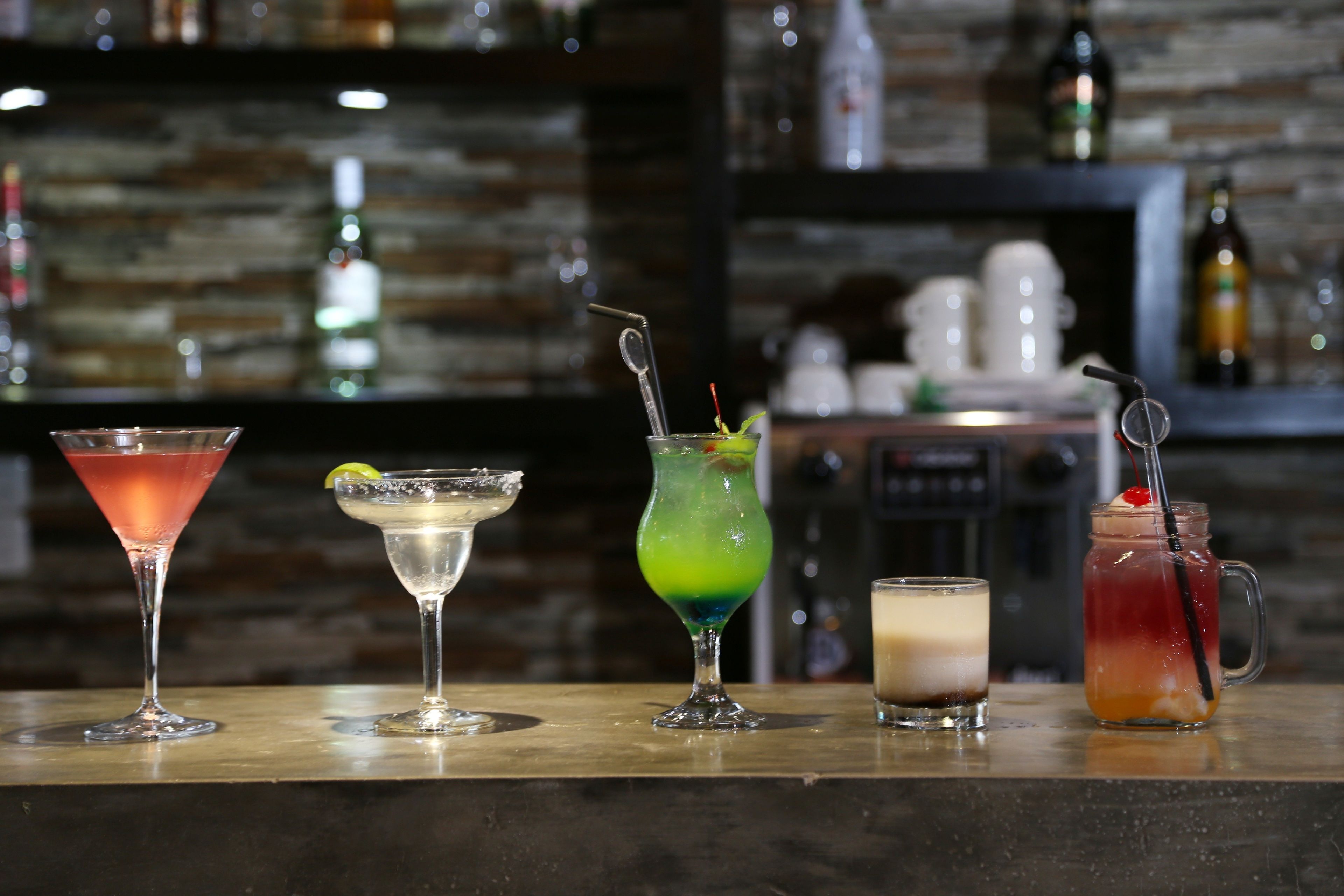 Eine Bar mit verschiedenen Getränken, darunter ein Martini, ein Margarita, ein Cocktail mit Limettengarnitur sowie ein Krug mit Trinkhalm.