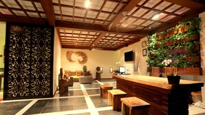 A reception area with a wooden reception desk, a wall-mounted plant display, a decorative wall panel, and a check-in counter. - The Jas Villas (Seminyak)