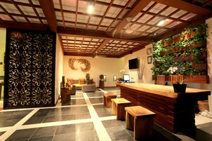 A reception area with a wooden reception desk, a wall-mounted plant display, a decorative wall panel, and a check-in counter.