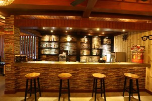A bar area with a stone wall, wooden bar counter, and three stools.