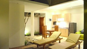 A modern kitchen with wooden cabinets, a refrigerator, and a dining area with a table and chairs. - The Jas Villas (Seminyak)