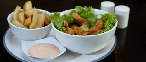 A table with two bowls of food, one containing fries and the other containing a salad with lettuce and breaded chicken pieces, and a small bowl of sauce.