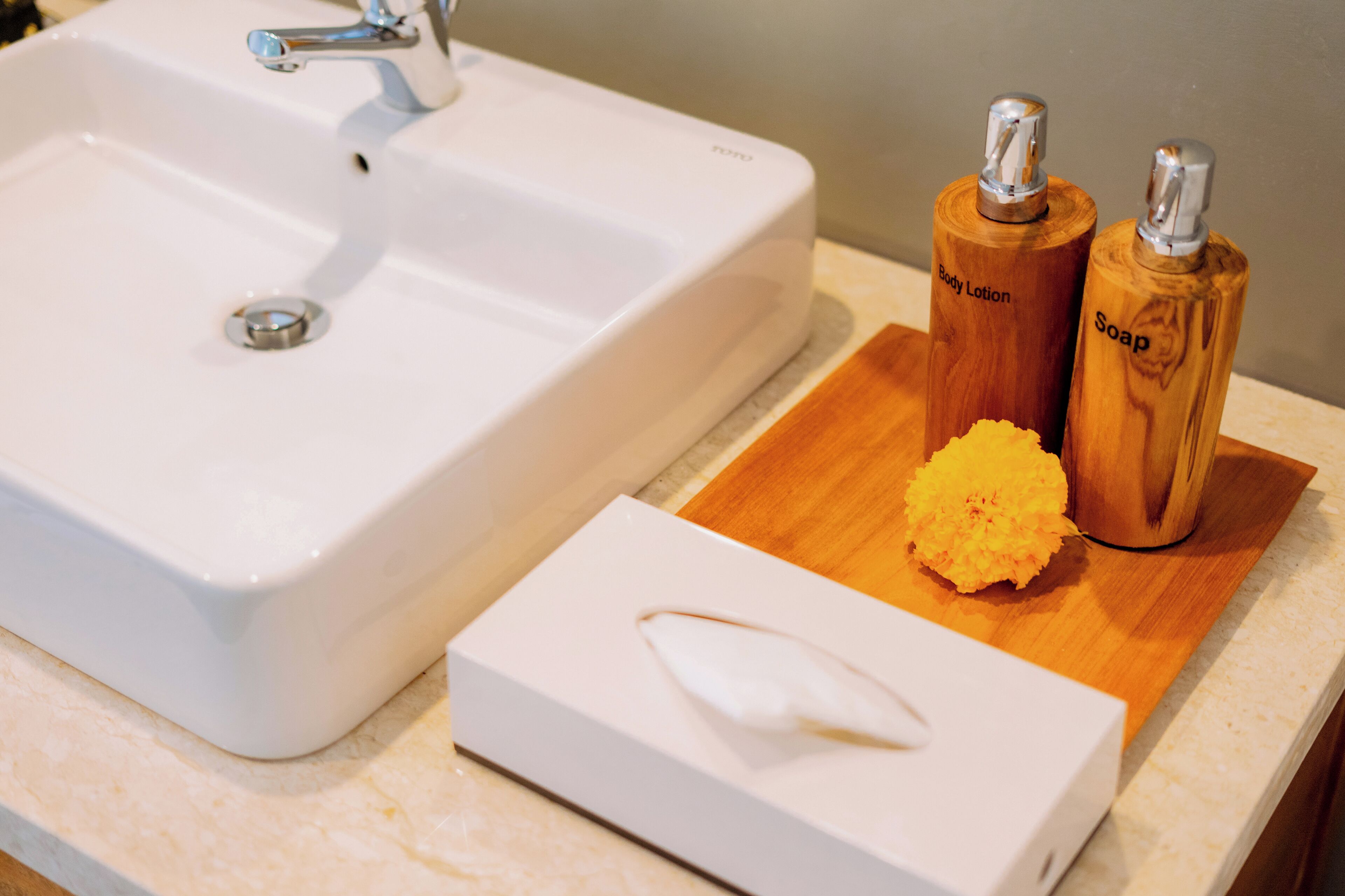 A bathroom sink with a wooden tray holding two soap bottles and a bar of soap.