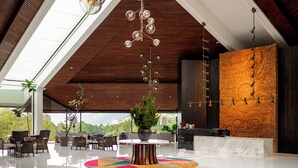 A modern lobby with a high ceiling, a central table with chairs, a reception desk, and a large window offering a view of the outdoors. - Handara Golf & Resort Bali (Bedugul)