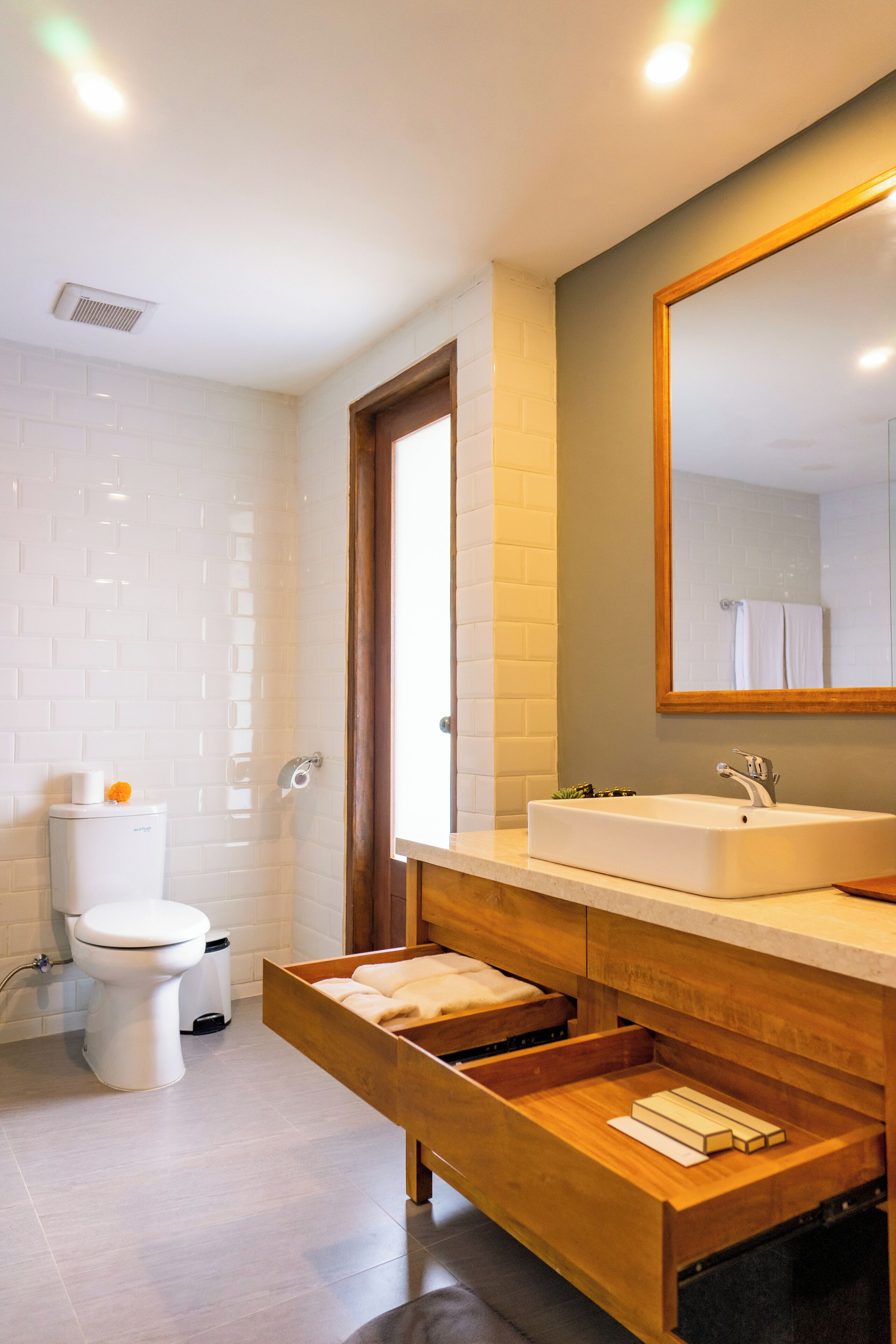 Un baño moderno con inodoro blanco, lavamanos con espejo y cajones de almacenamiento de madera.