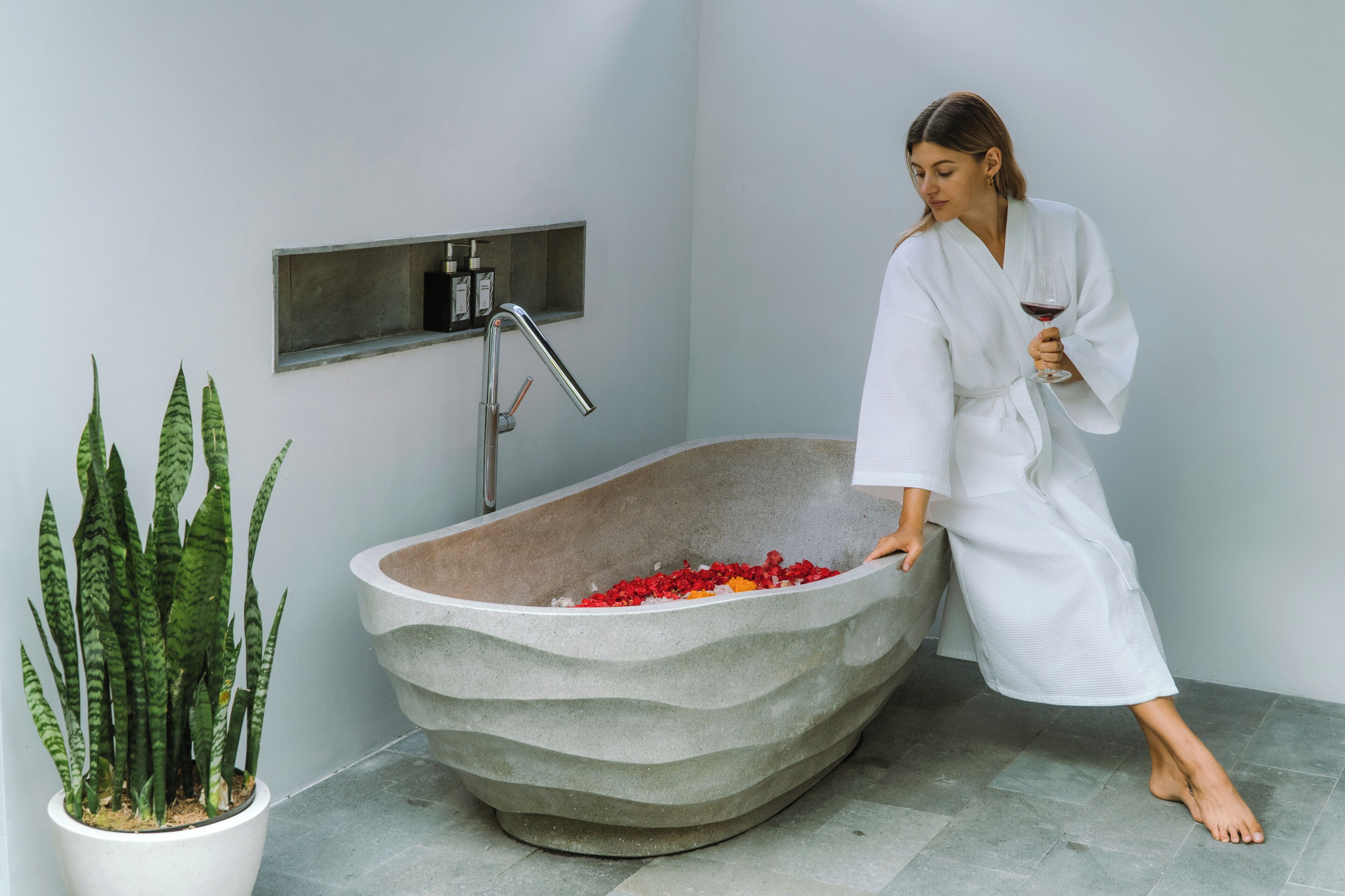 A modern bathroom with a freestanding bathtub, a potted plant, and a wall-mounted faucet.