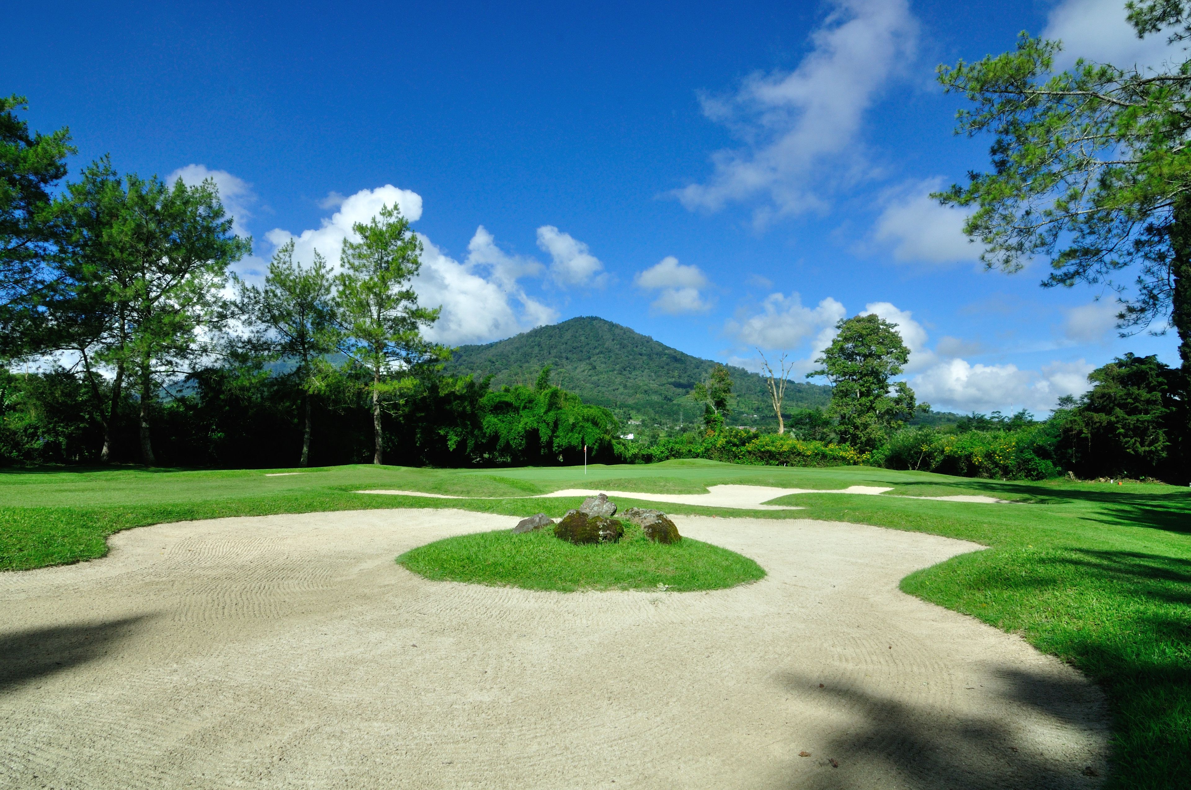 A golf course with sand bunkers, a flagstick, and a mountain in the background.