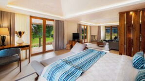 A modern hotel room with a large bed, a desk, a TV, and a view of the garden. - Handara Golf & Resort Bali (Bedugul)