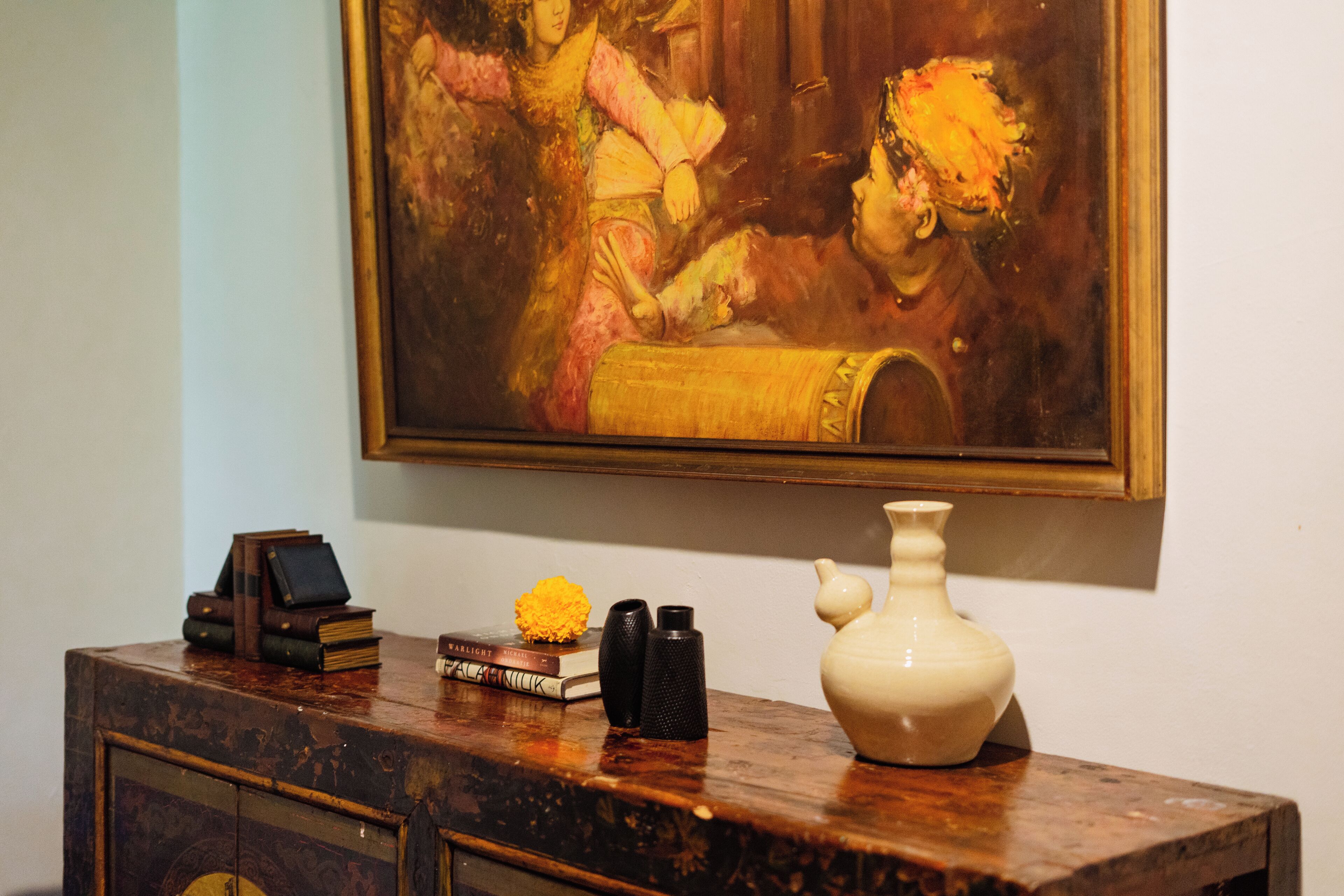 A wooden dresser with a painting above it, a vase, books, and decorative items.