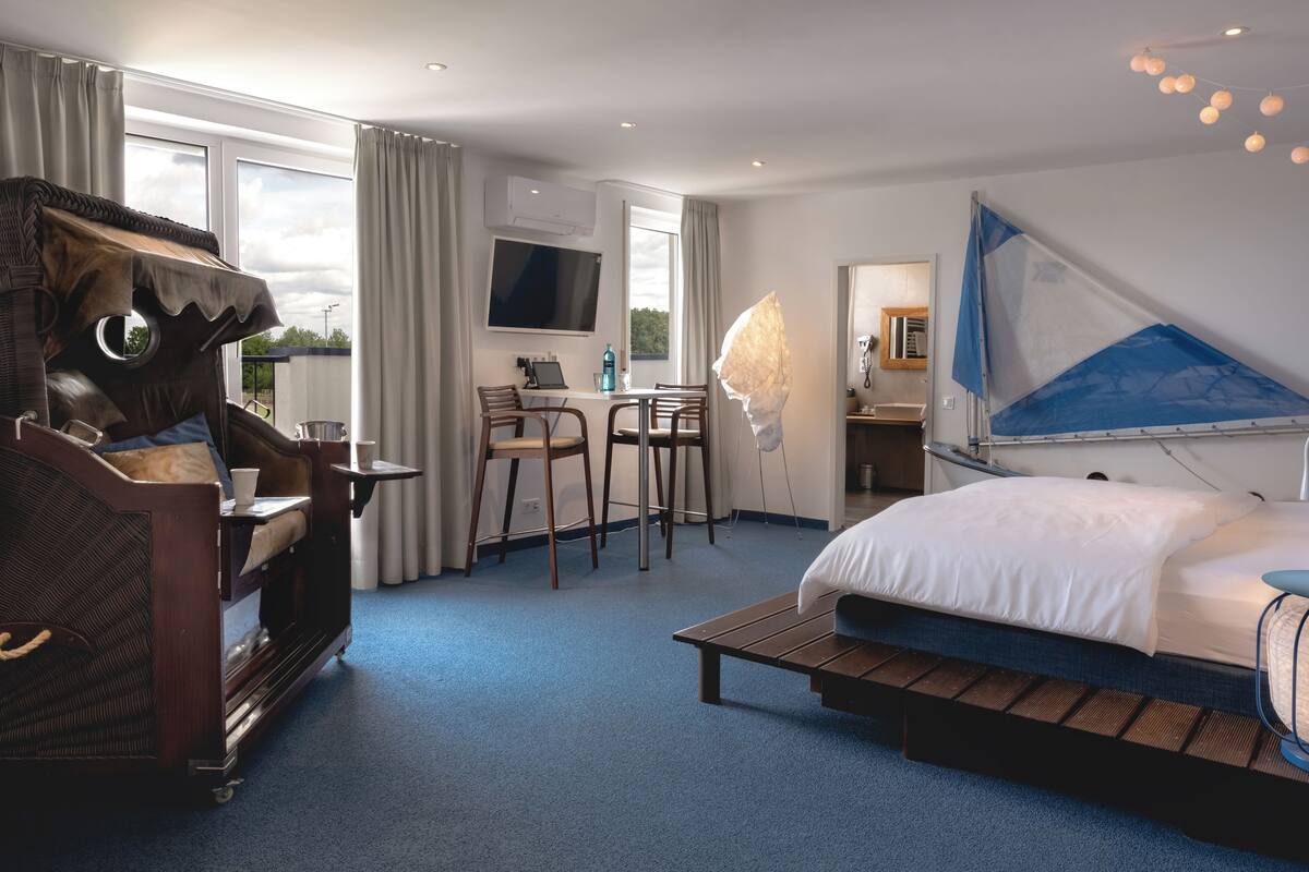 A hotel room with a bed, a desk with a chair, a coffee machine, and a large window.