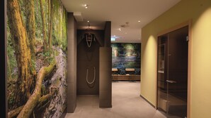 A hallway with a forest mural, a glass door, and a bench with a view of a water feature. - Sport- & Seminarhotel Glockenspitze (Altenkirchen)