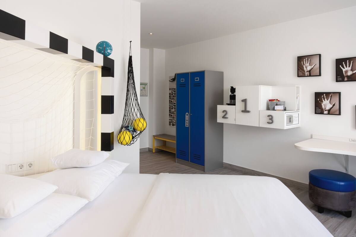 A modern hotel room with a large bed, a hanging chair, a desk, and lockers.