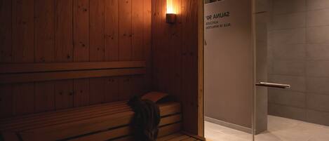 A wooden sauna with benches, a glass door, and a wall-mounted light.