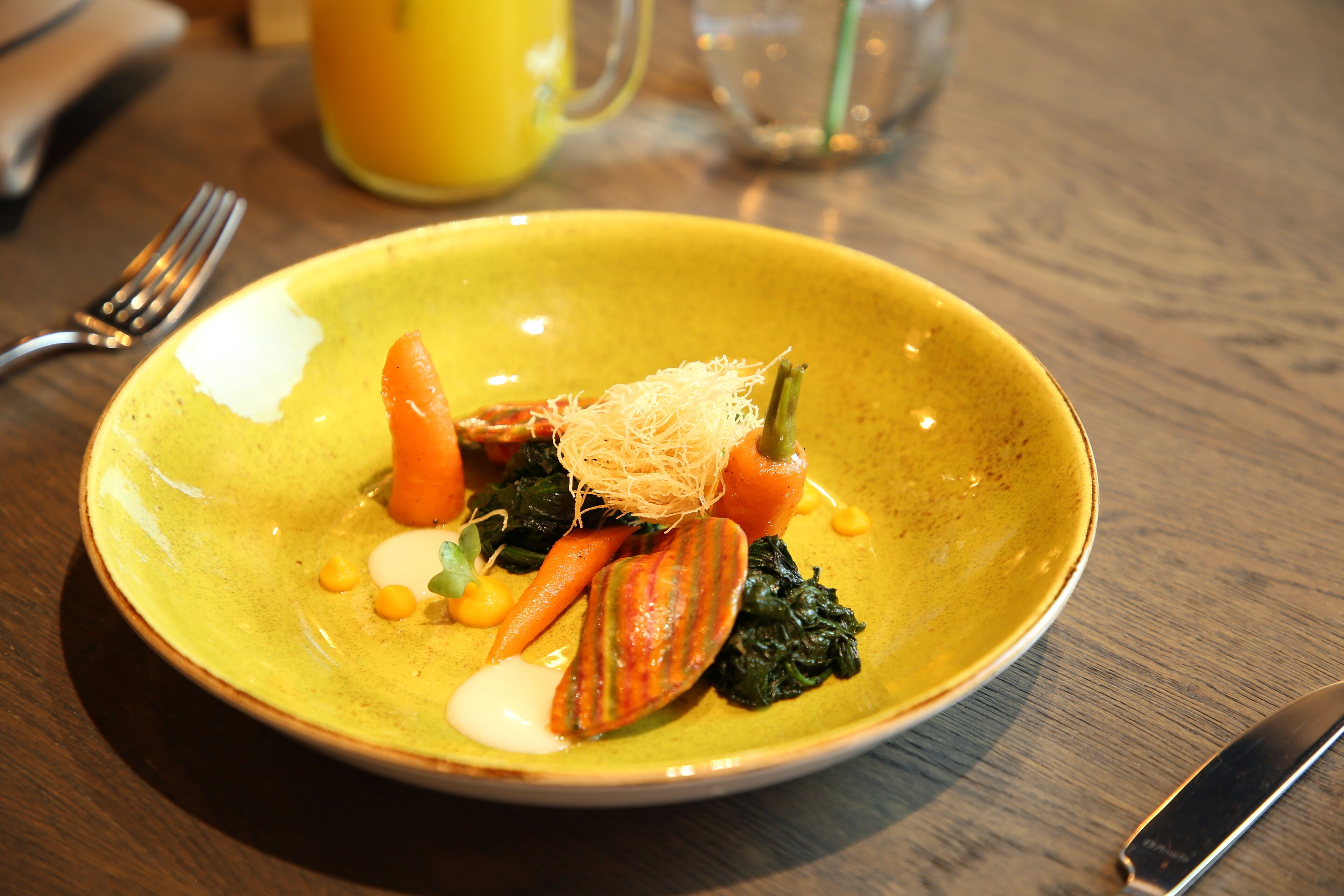 Un plato amarillo con una variedad de verduras y un trozo de pescado sobre una mesa de madera.