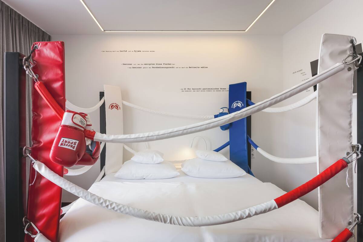 A boxing ring with white and red padding, ropes, and a punching bag.