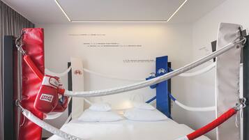 A boxing ring with white and red padding, ropes, and a punching bag.