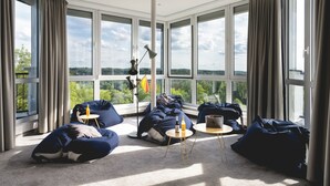 A spacious room with large windows, bean bags, a small round table, and a lamp. - Sport- & Seminarhotel Glockenspitze (Altenkirchen)