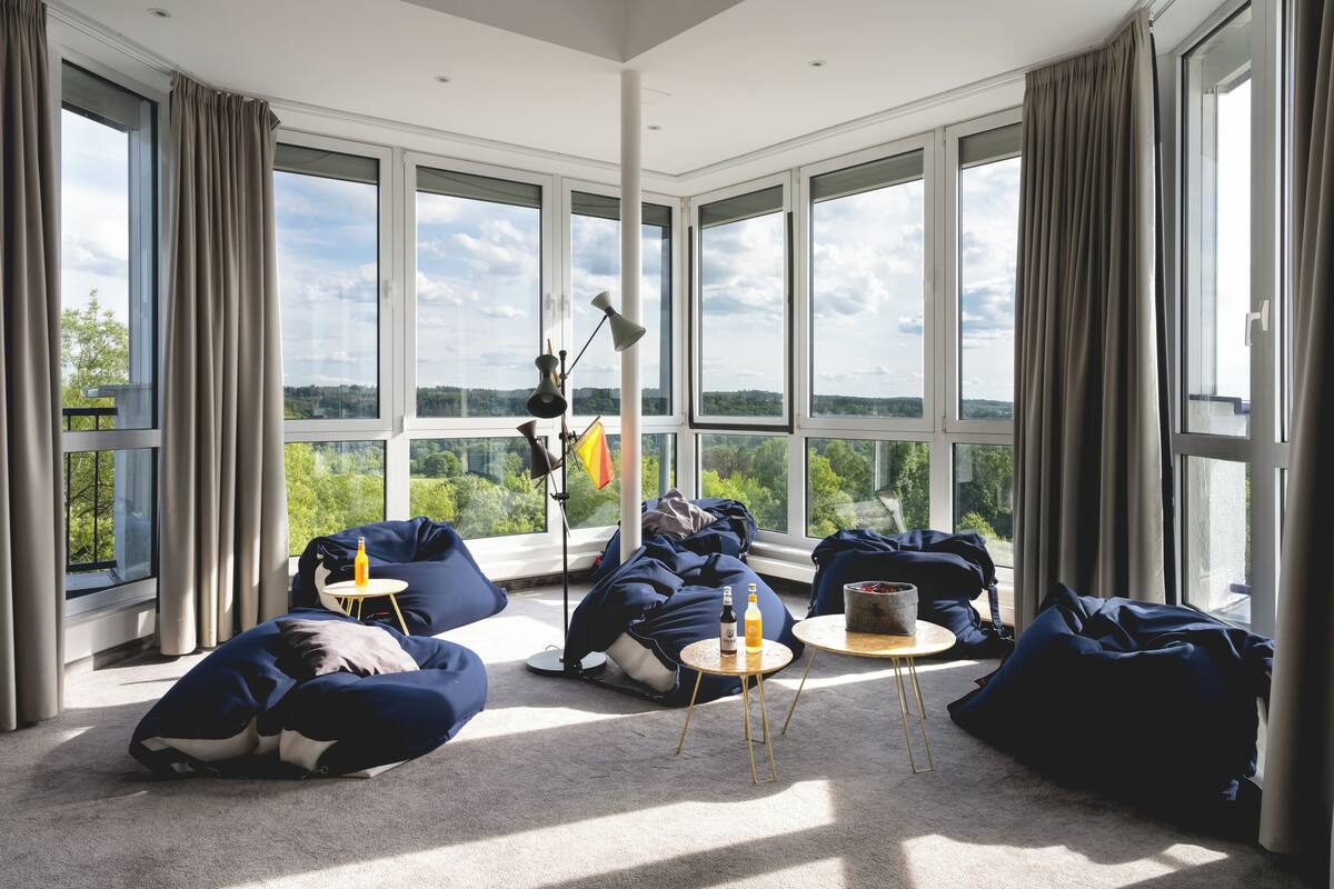 A spacious room with large windows, bean bags, a small round table, and a lamp.
