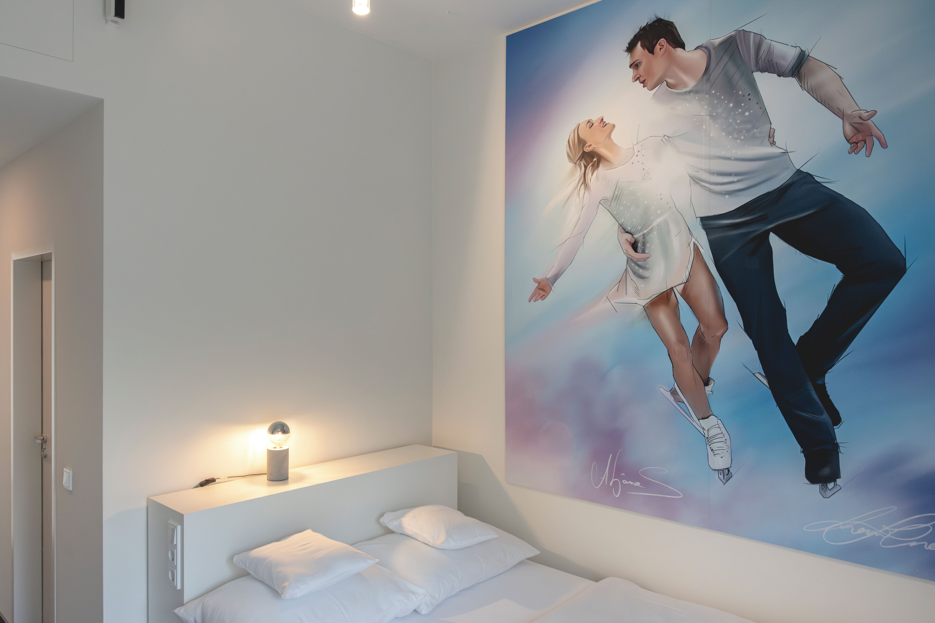 Un dormitorio con cama, una mesita de noche con lámpara y un cartel grande de una pareja bailando en la pared.