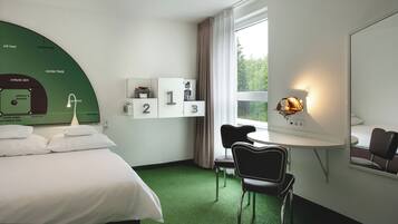 Habitación de hotel con cama, escritorio, silla, ventana con cortinas y un cartel con número en la pared.