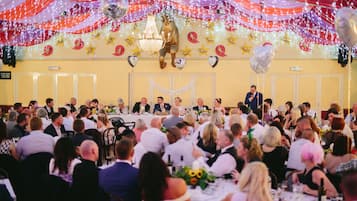 Un salón de banquetes con mesas redondas y comensales sentados.