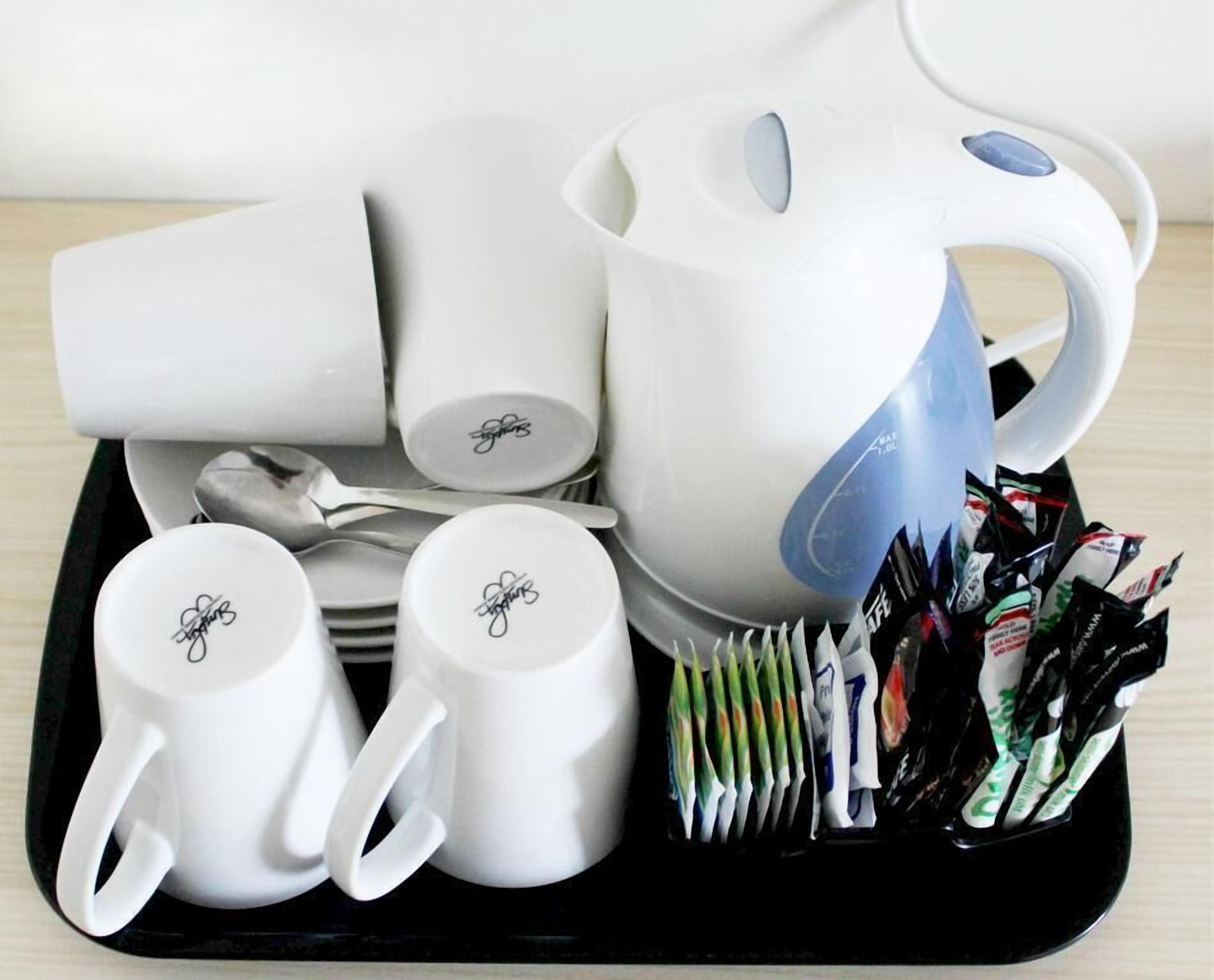 A tray with a white teapot, two white cups, a stack of white plates, and a black tray.