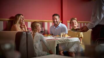 Une famille est assise à une table dans un restaurant. Le mur est rouge et les bancs sont à rayures.