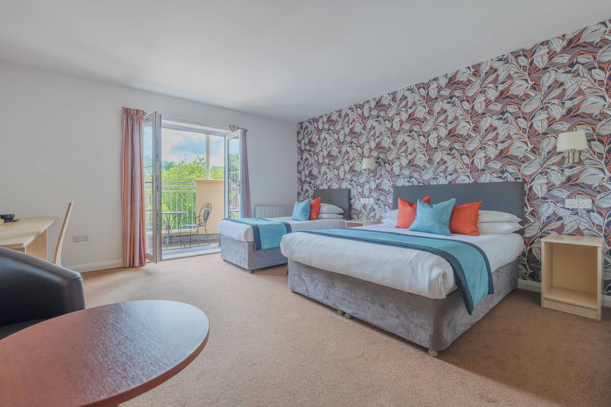 A hotel room with two beds, a balcony, a desk, and a patterned wall.