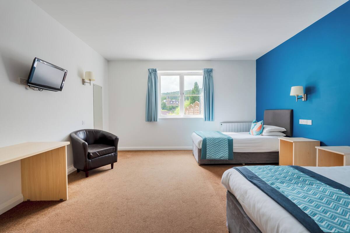 A hotel room with a bed, a desk, a chair, a TV, and a window with curtains.