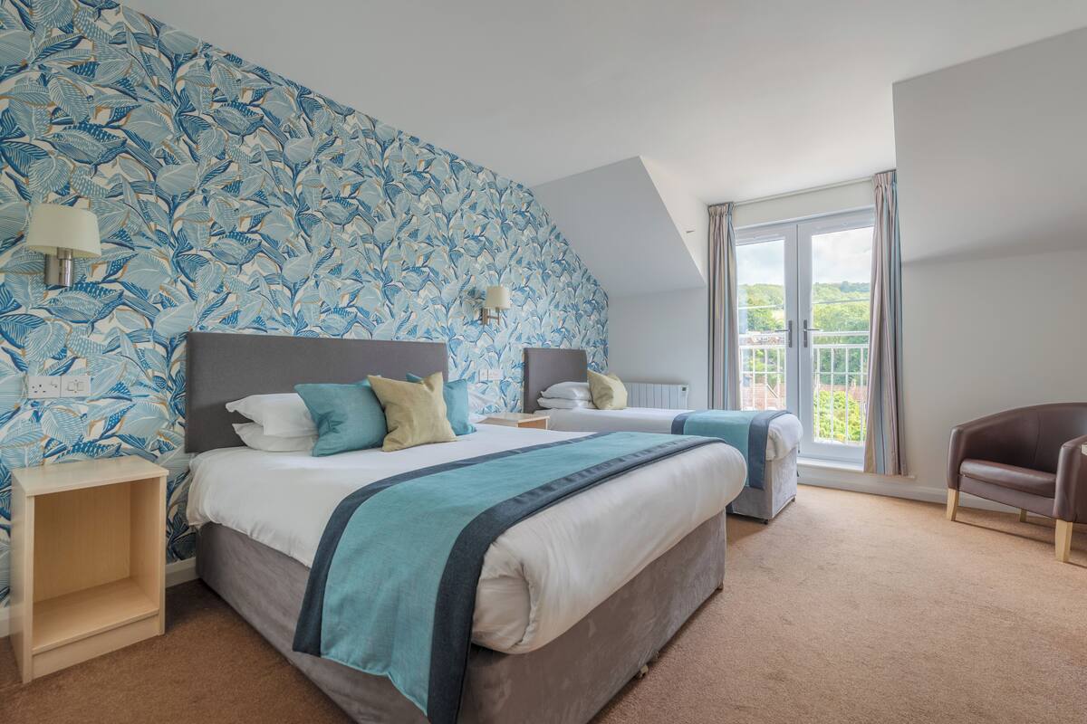 A bedroom with two beds, a large window, and a view of greenery outside.