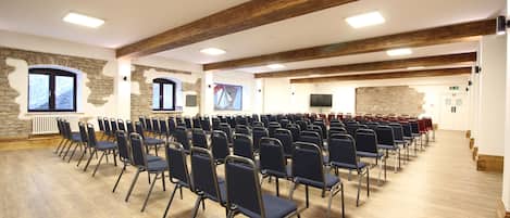 Un salón de conferencias con filas de sillas plegables, paredes de piedra, vigas de madera y una chimenea.