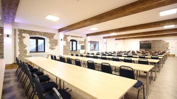 Un salón de conferencias con largas mesas y sillas, paredes de piedra y vigas de madera.