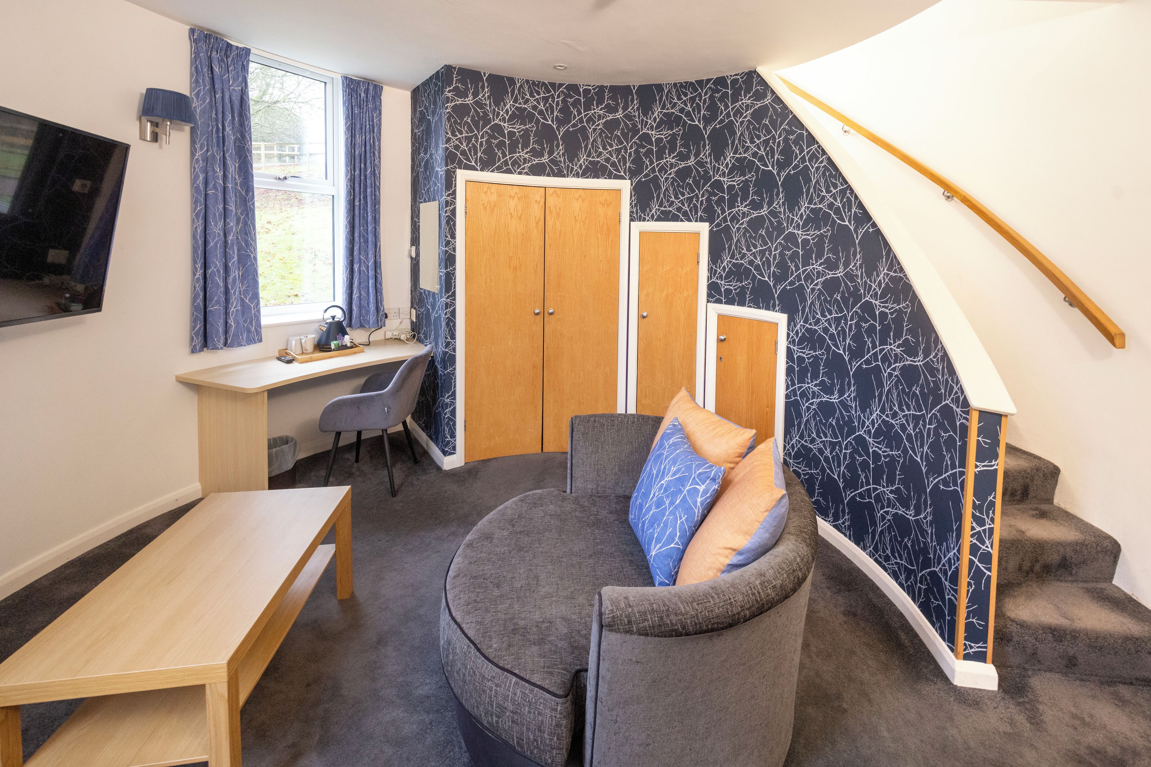 Ein kleines Zimmer mit Schreibtisch, einer gebogenen Couch und einer Treppe.