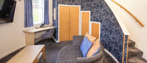 Ein kleines Zimmer mit Schreibtisch, einer gebogenen Couch und einer Treppe.