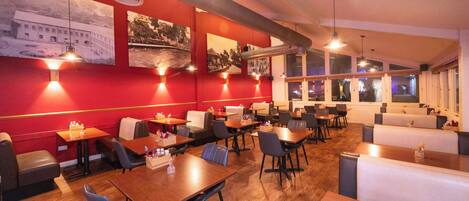 Un interior de restaurante con cabinas, mesas y una pared roja decorada con fotografías históricas.