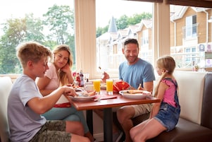 Una familia desayunando en una mesa con vistas a un edificio que tiene una torre y una ventana con persianas.