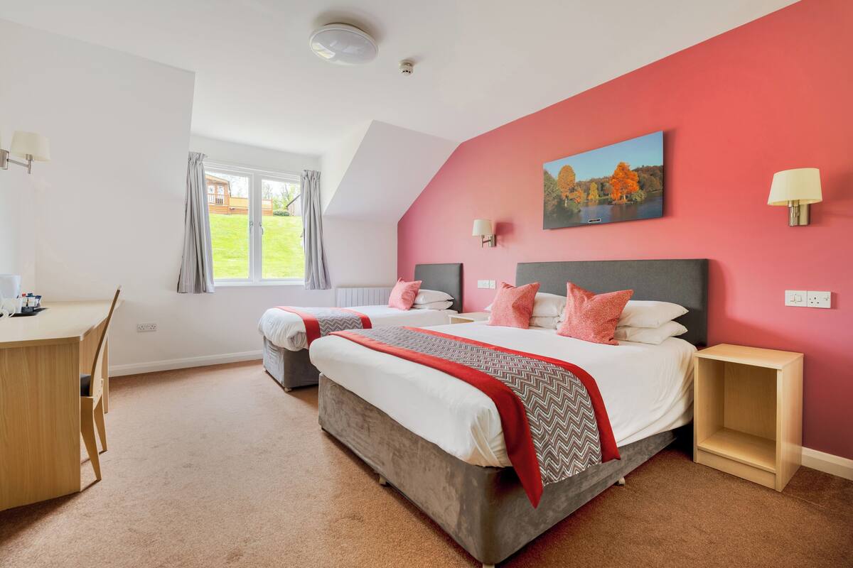 A bedroom with a large bed, two bedside tables, a desk, and a window with curtains.