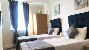A hotel room with two beds, a wardrobe, a painting, and a window with curtains.