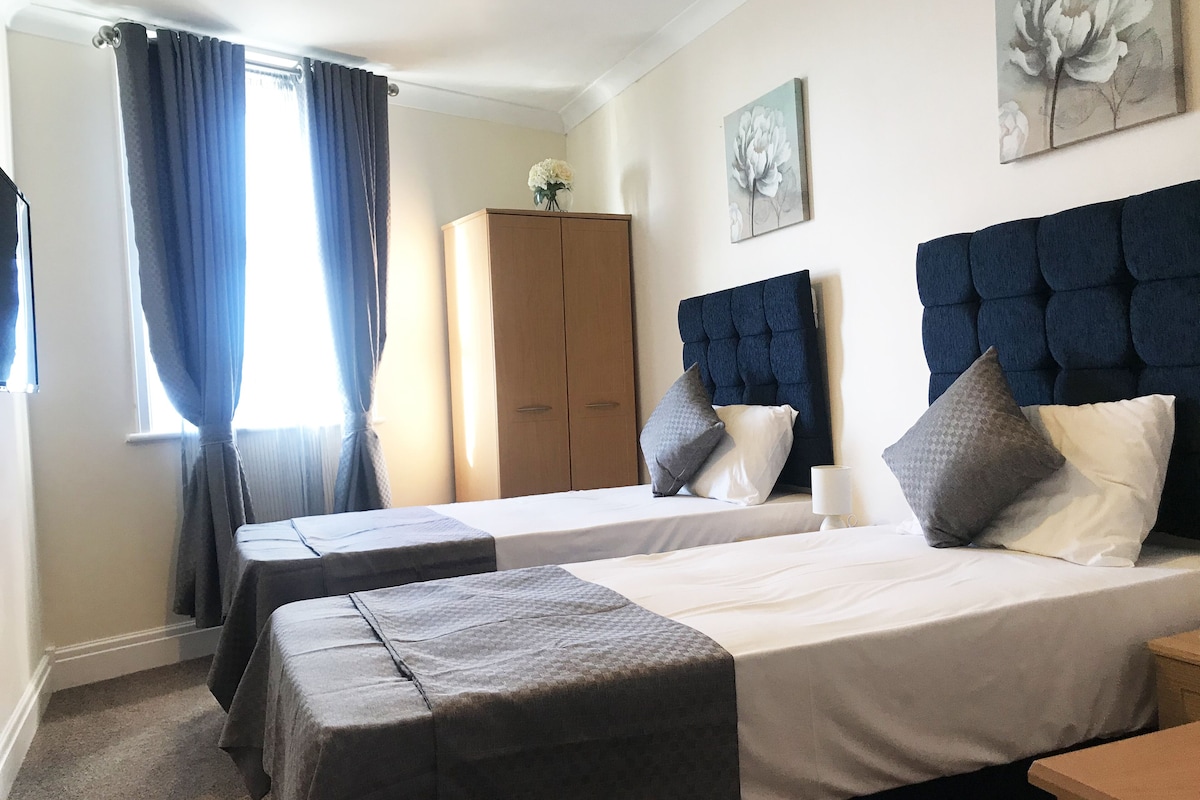 Una habitación de hotel con dos camas, un armario, un cuadro y una ventana con cortinas.