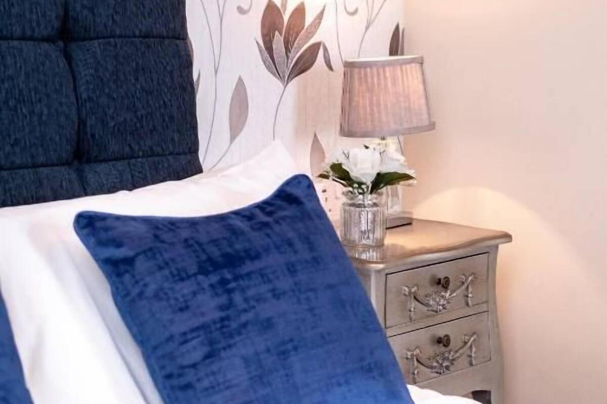 Un llit amb almoades blaves, una làmpada de nit i una paret decorativa.