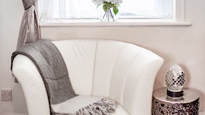 A white armchair with a gray throw blanket, a decorative vase with white flowers, and a patterned side table.
