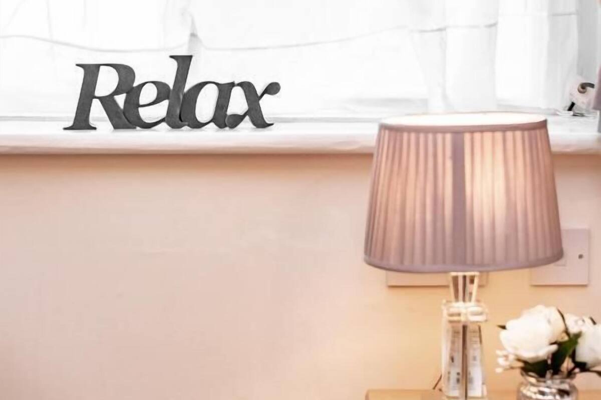 Habitació amb finestra, una làmpada i la paraula 'Relax' decorativa a la paret.