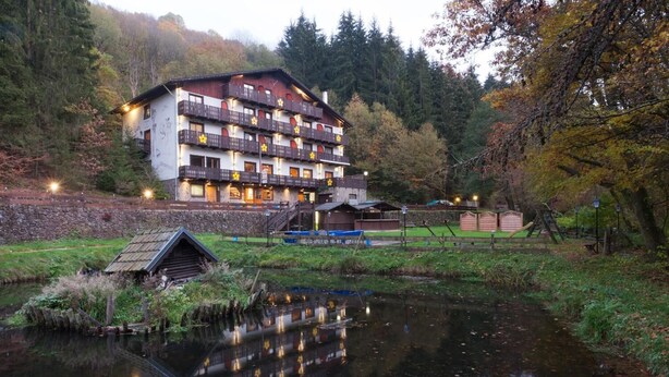 A multi-story hotel with balconies, a small dock, and a reflection in the water. - Wolffhotel (Kopp)