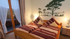 A double bed with striped bedding, a wooden headboard, a nightstand with a lamp, and a wall-mounted tree decoration. - Wolffhotel (Kopp)
