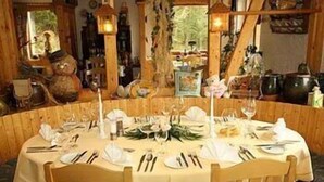 A round dining table set for four with white tablecloths, wooden chairs, and a floral centerpiece. - Wolffhotel (Kopp)