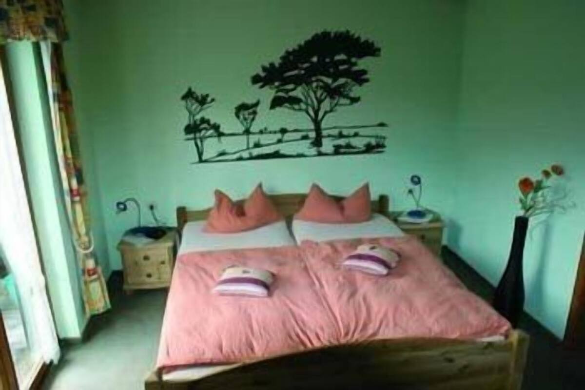 A bedroom with a bed, two nightstands, a wall decoration, and a window with curtains.