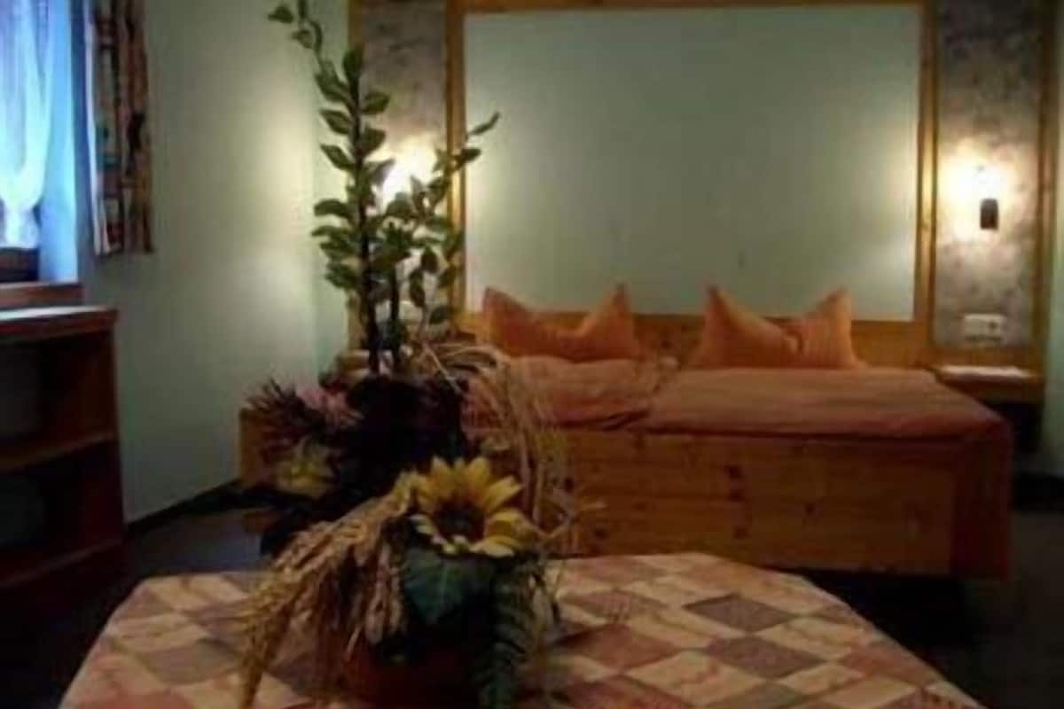 A bedroom with a bed, a nightstand, a wall-mounted lamp, and a decorative plant.