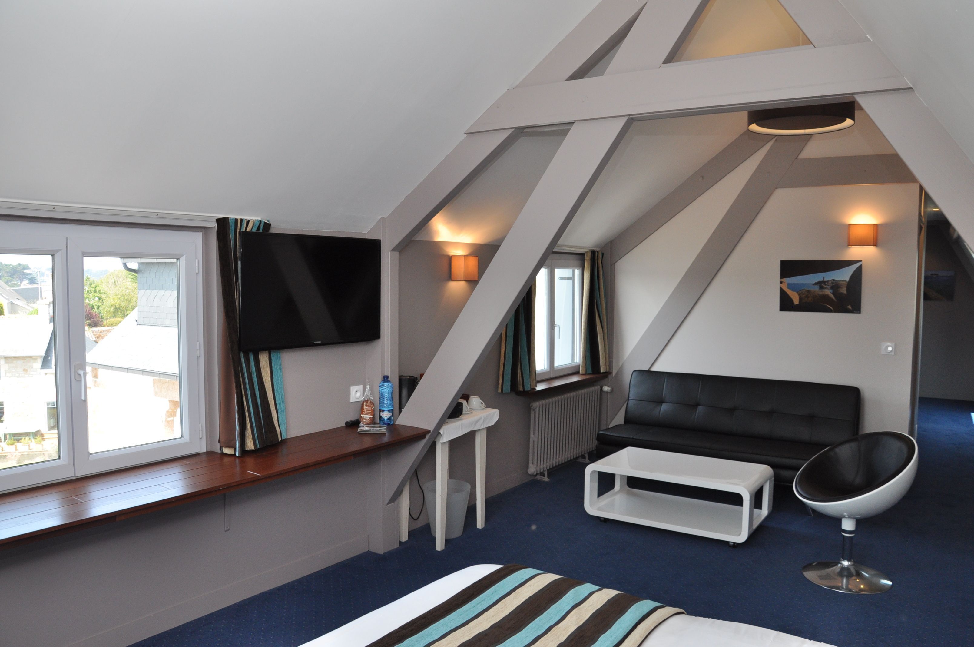 Une chambre de style loft moderne, dotée d’une grande fenêtre, d’un téléviseur à écran plat, d’un canapé en cuir noir, d’une table basse blanche et d’un fauteuil original en forme d’œuf.